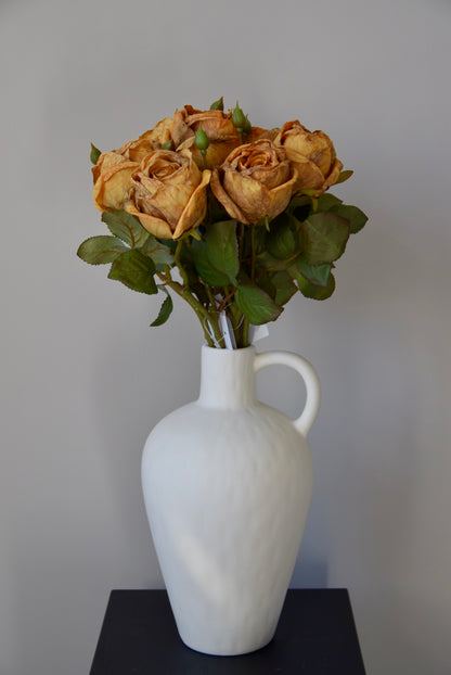 White vase with a bouquet of roses on a black surface against a grey background