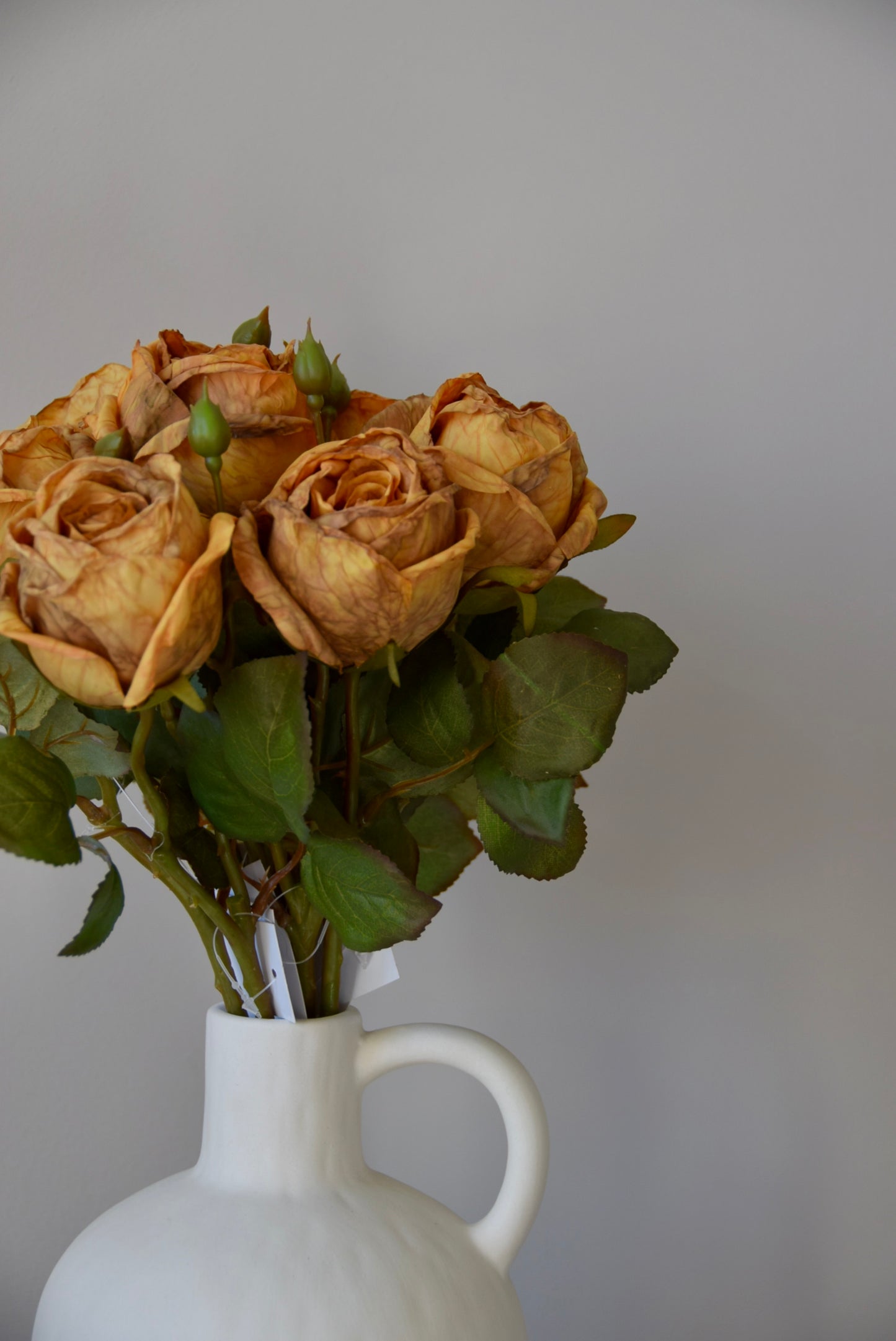 Bouquet of dried roses in a white vase against a plain background
