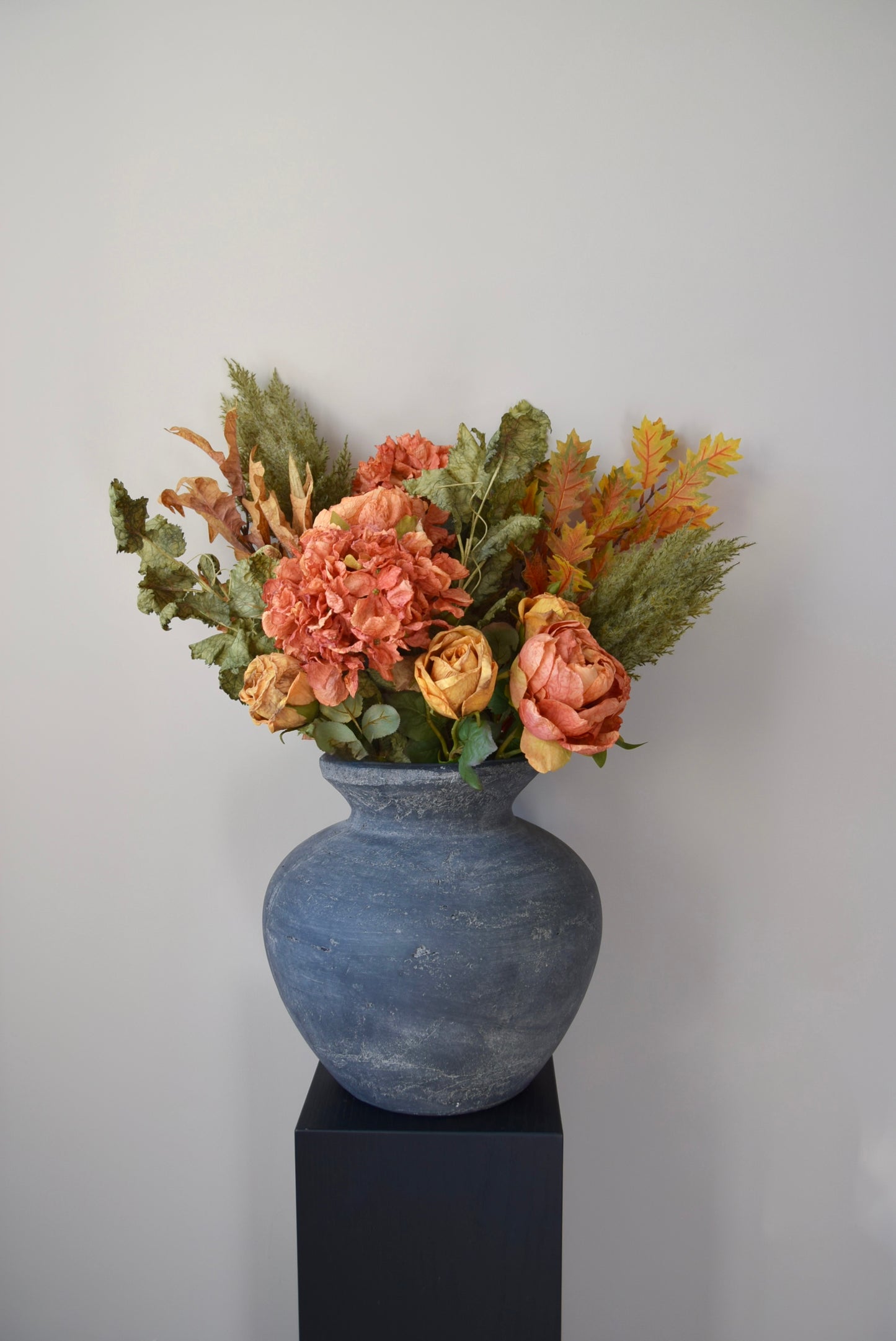 Decorative vase with artificial flowers on a black pedestal against a plain background