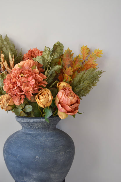 Grey vase with autumn-themed flowers against a plain background