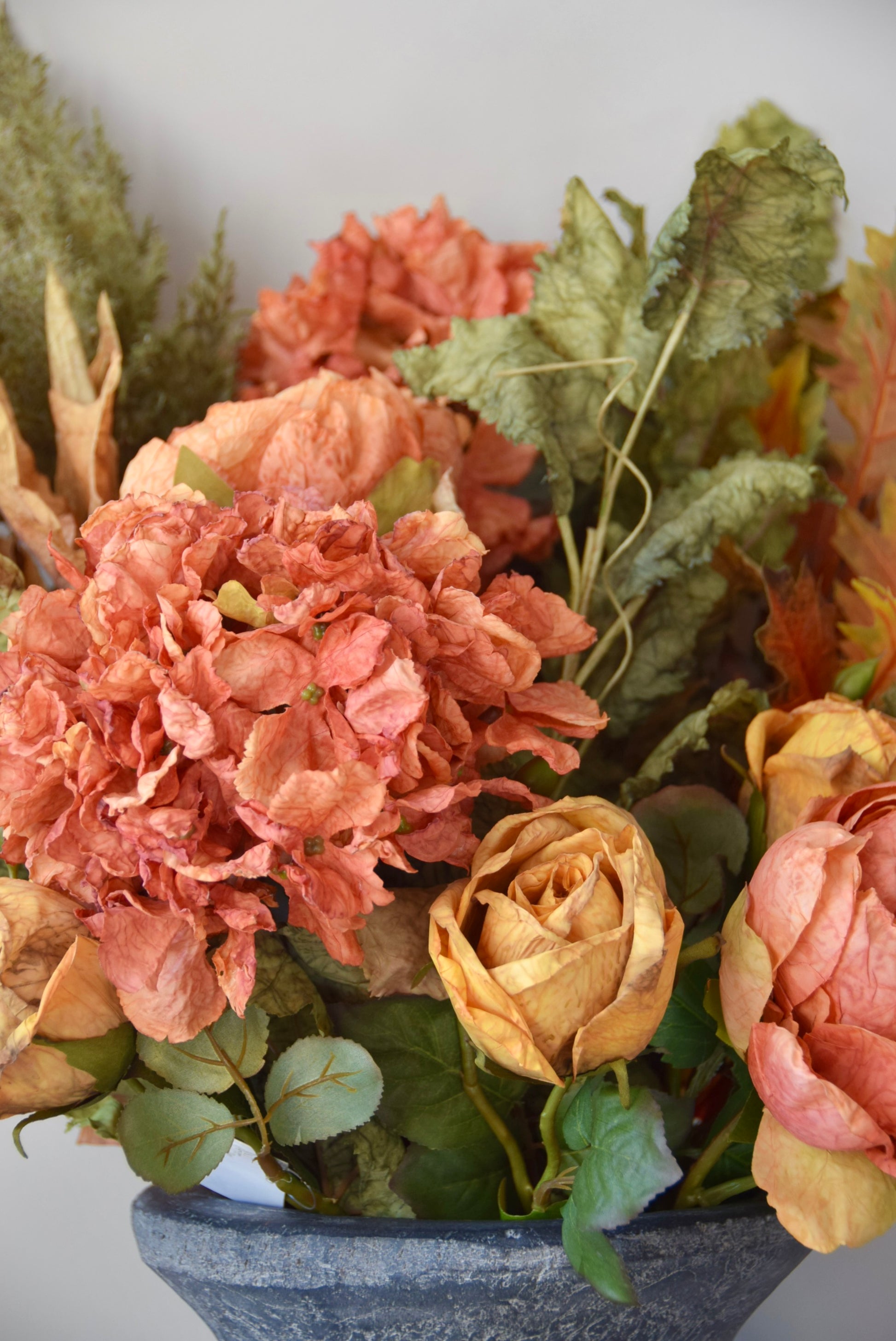 Artificial flower arrangement with orange and yellow flowers in a grey pot on a white background