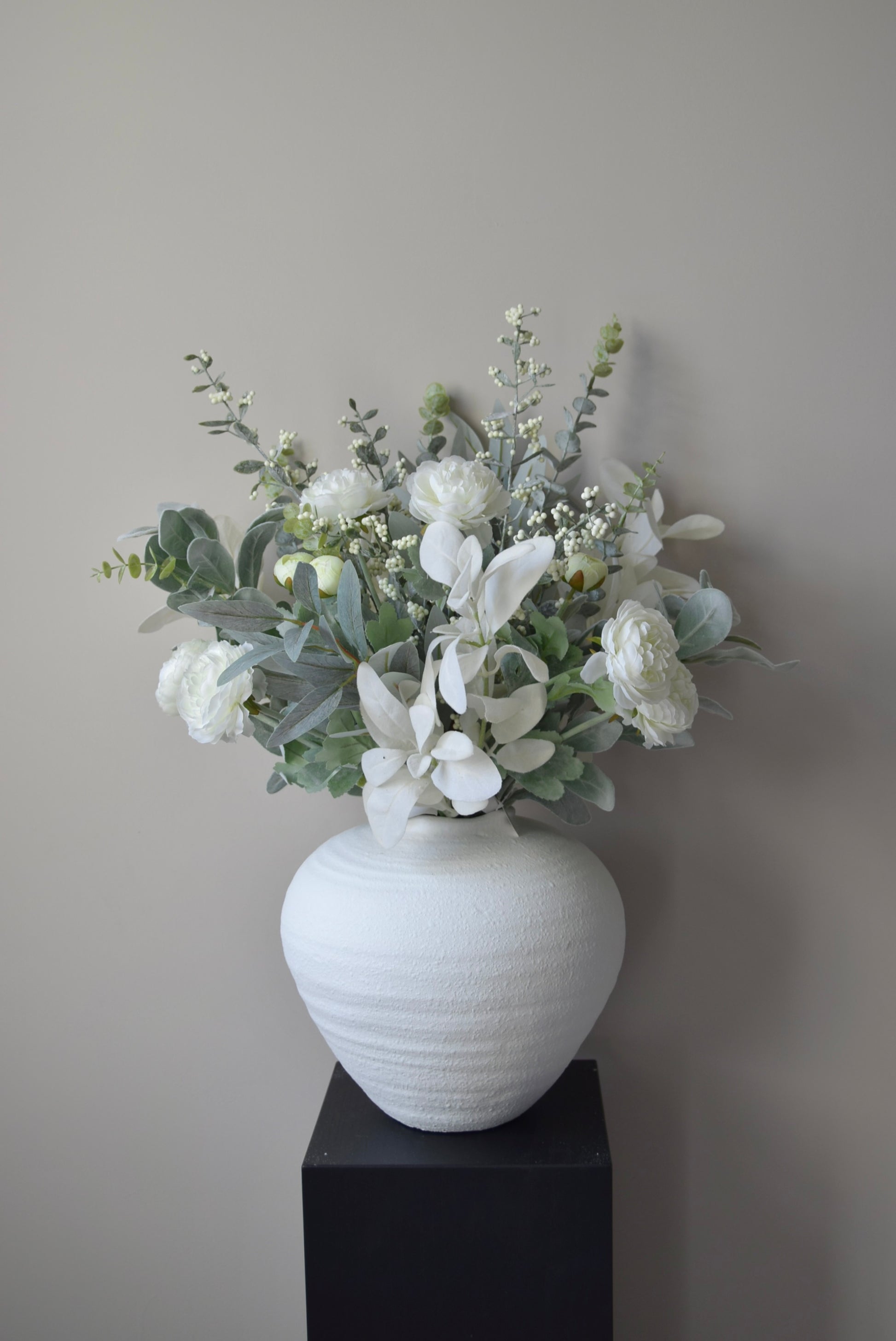 White vase with a bouquet of flowers on a black pedestal against a neutral wall