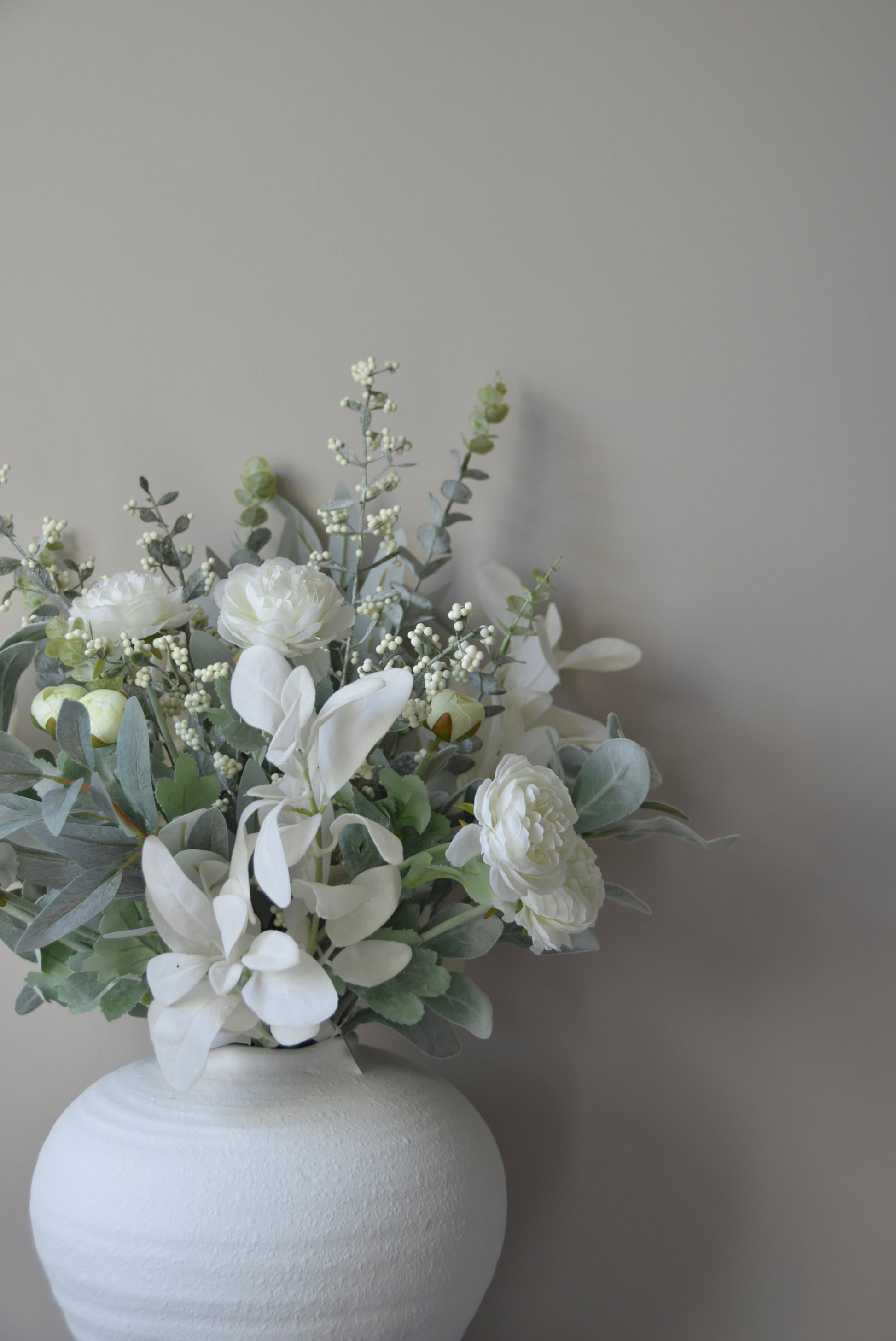 White vase with a bouquet of flowers against a plain wall