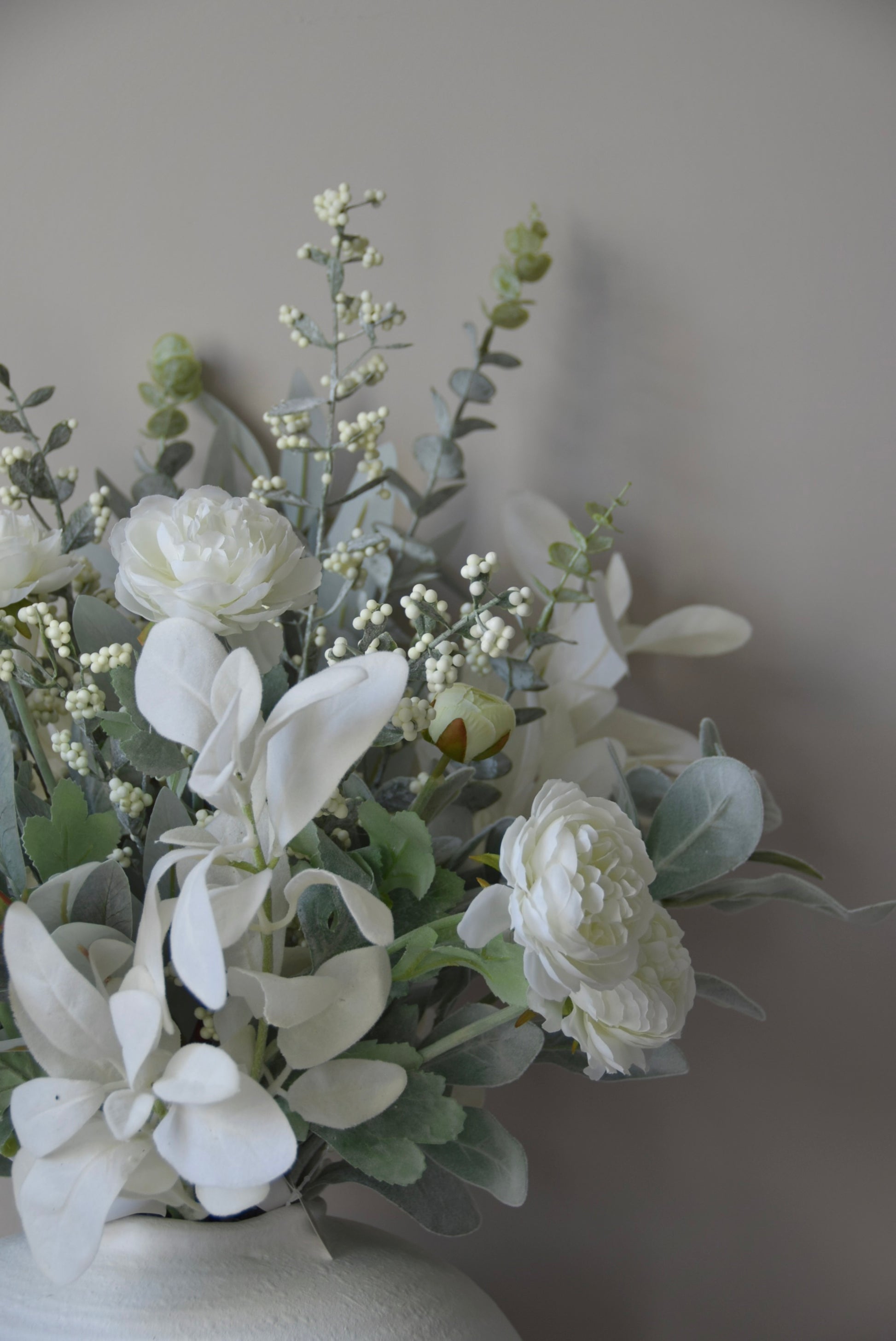 Artificial white flowers in a vase against a plain background