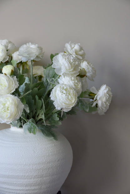 White flowers in a textured white vase against a plain background