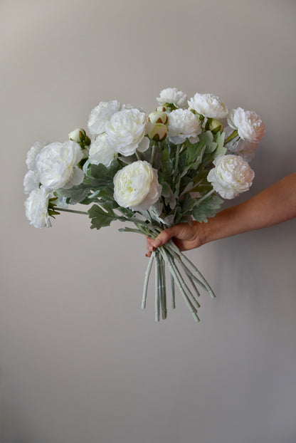 Bouquet of white flowers held by a hand against a plain background