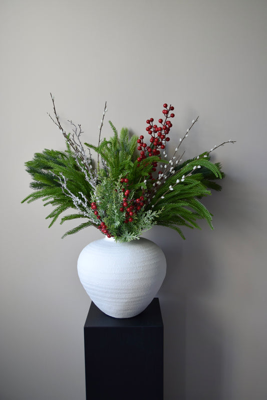 White vase with greenery and red berries on a black pedestal against a grey background