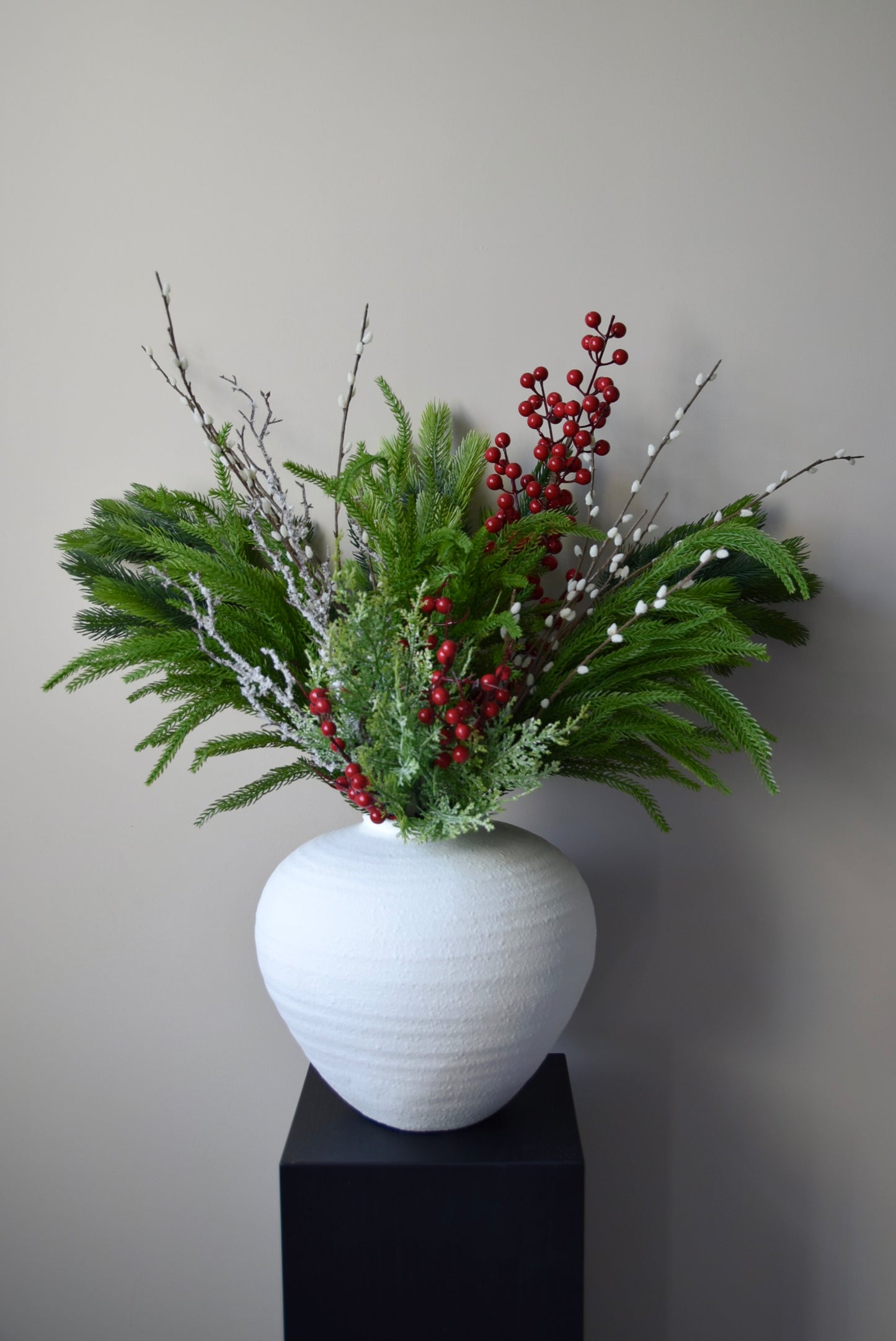 White vase with greenery and red berries on a grey background