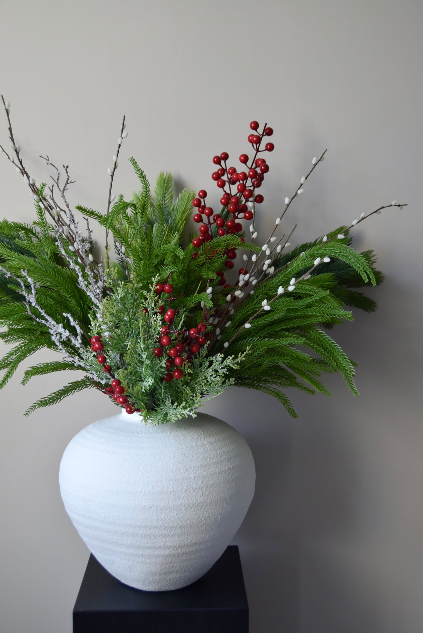 White vase with greenery and red berries on a grey background