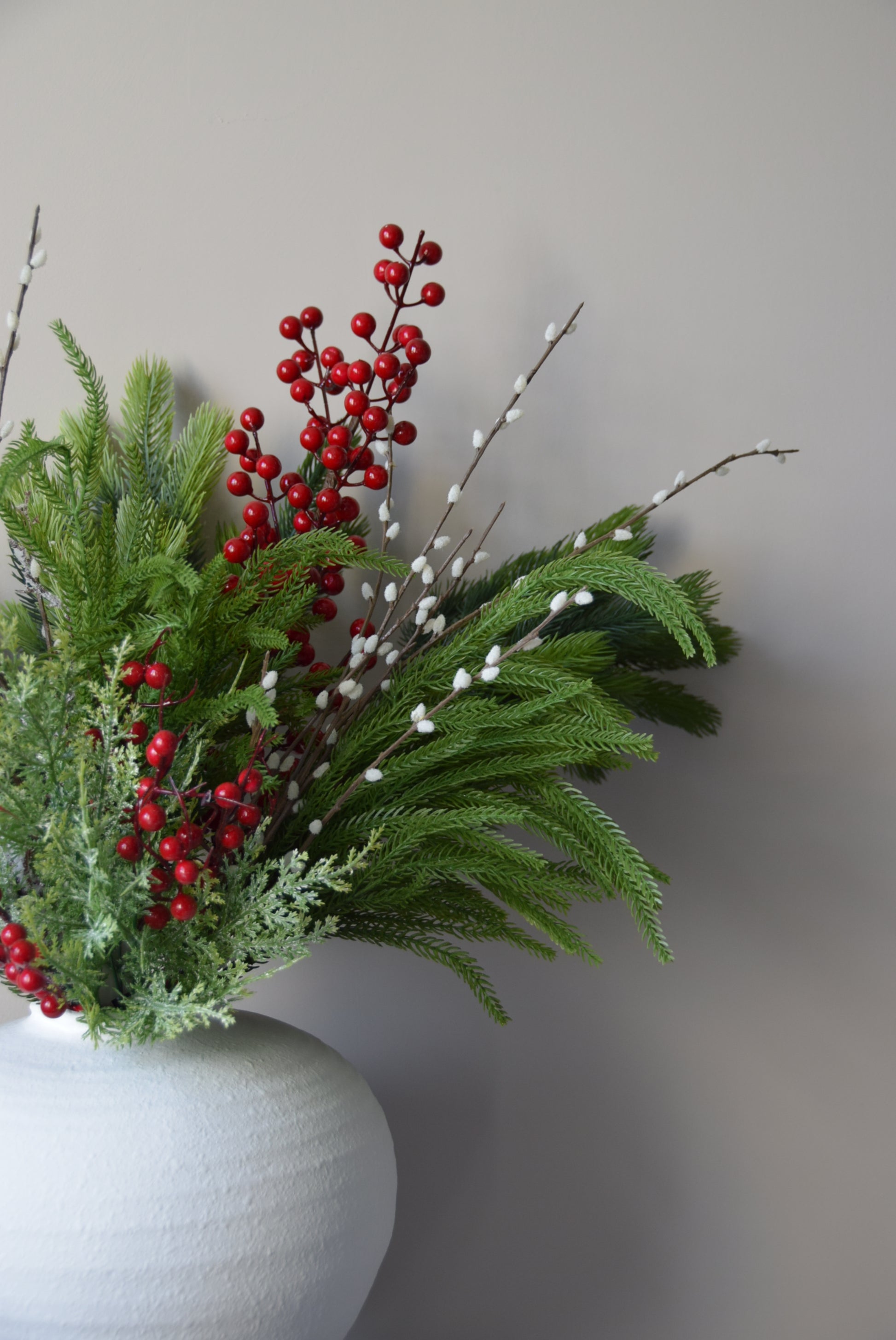 Decorative arrangement of greenery and red berries against a neutral background