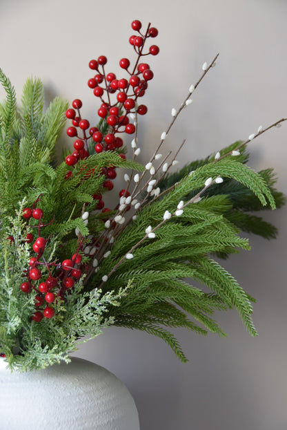 Decorative arrangement of greenery with red berries and white stems on a neutral background