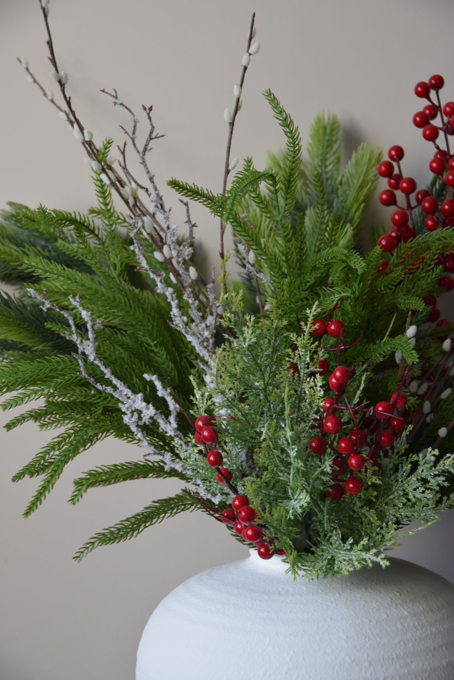Decorative arrangement of greenery with red berries on a neutral background