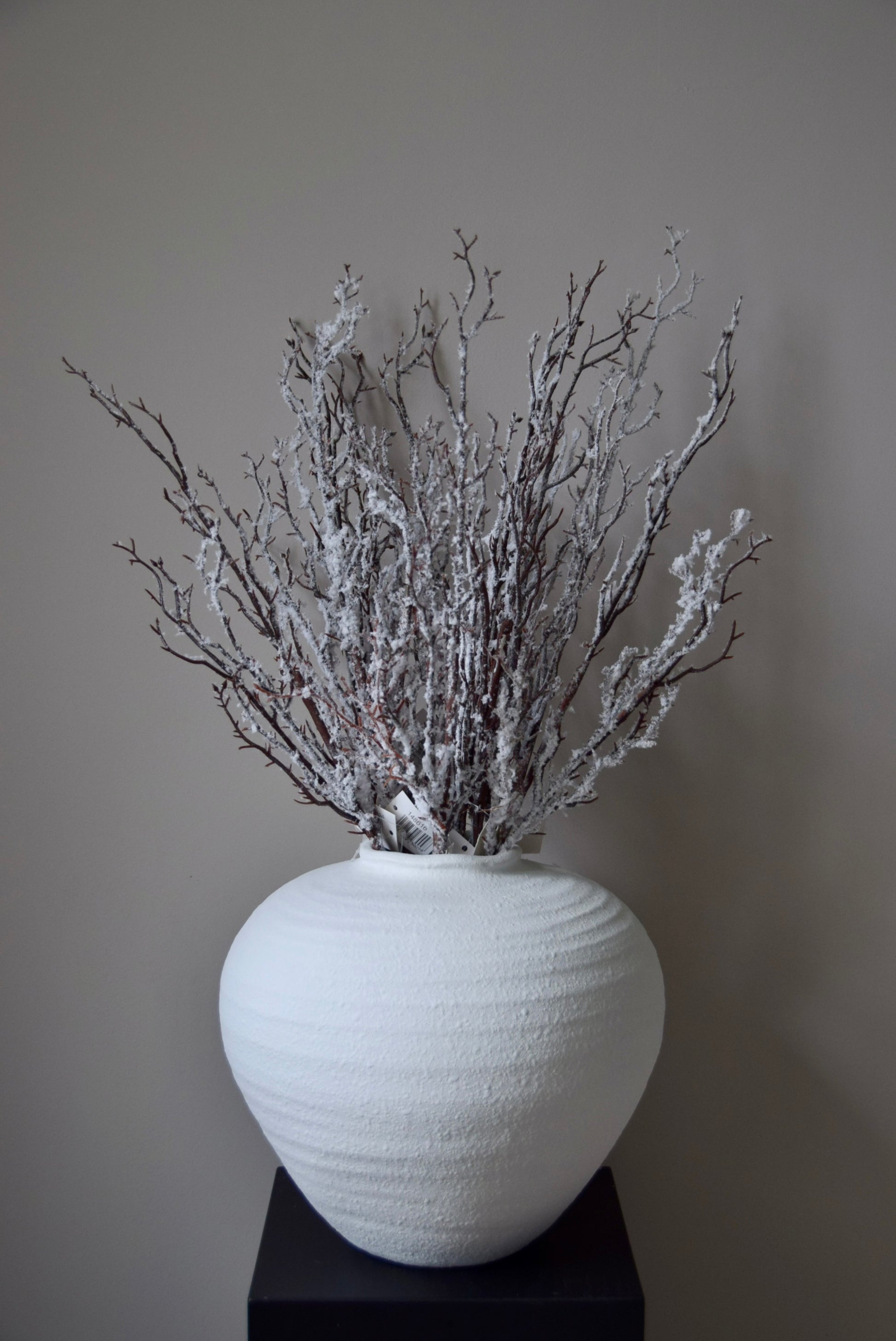 White textured vase with dried snowy branches against a plain background
