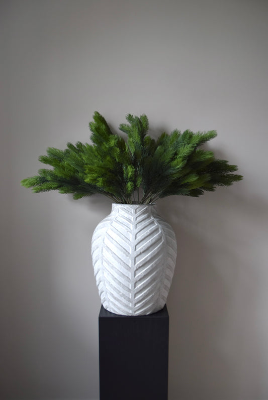 White textured vase with green spruce branch against a grey background