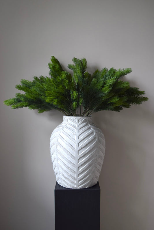 White textured vase with green foliage against a grey background