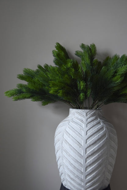 White textured vase with green spruce branch against a plain background