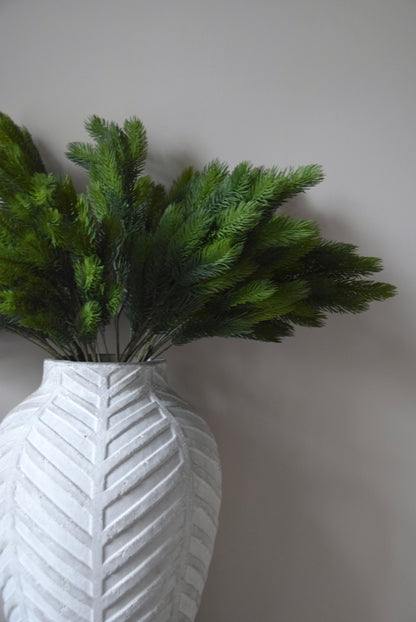 White textured vase with green foliage against a plain background