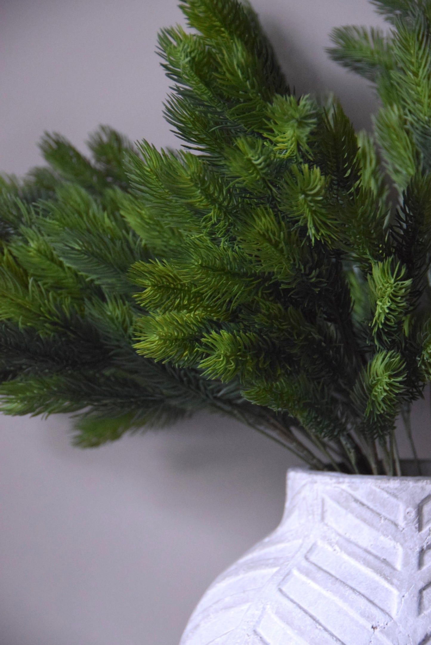 Artificial green spruce in a white textured vase on a light grey background
