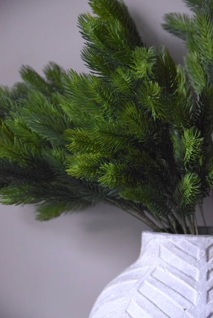 Artificial green spruce in a white textured vase on a light grey background