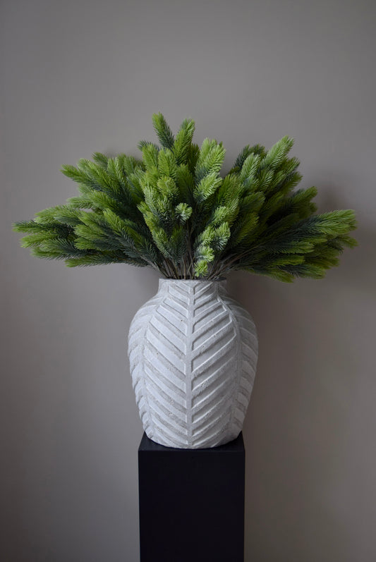 White textured vase with green foliage against a grey background