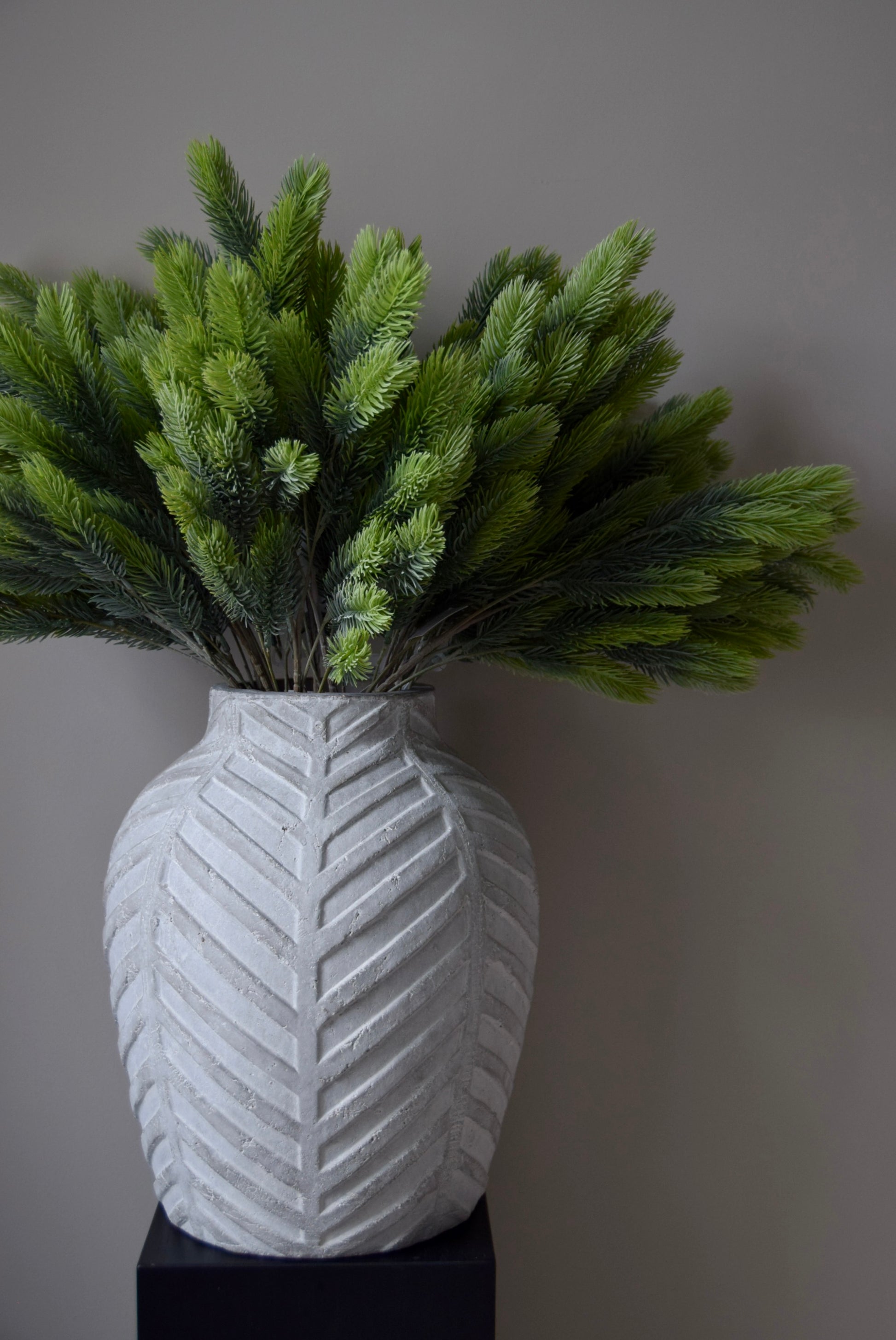 White textured vase with green foliage against a grey background