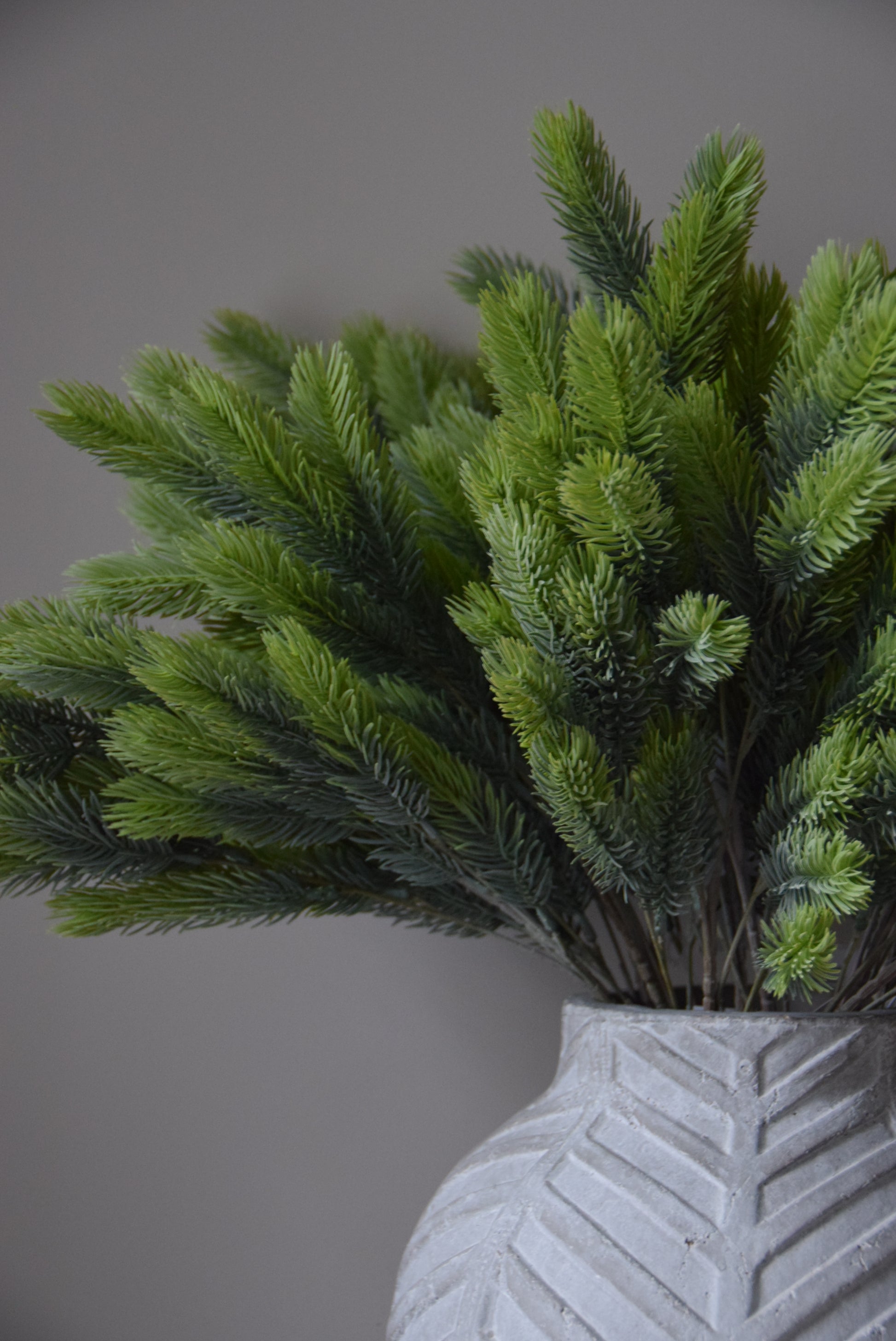 Artificial Christmas tree branch with a textured grey base on a plain background