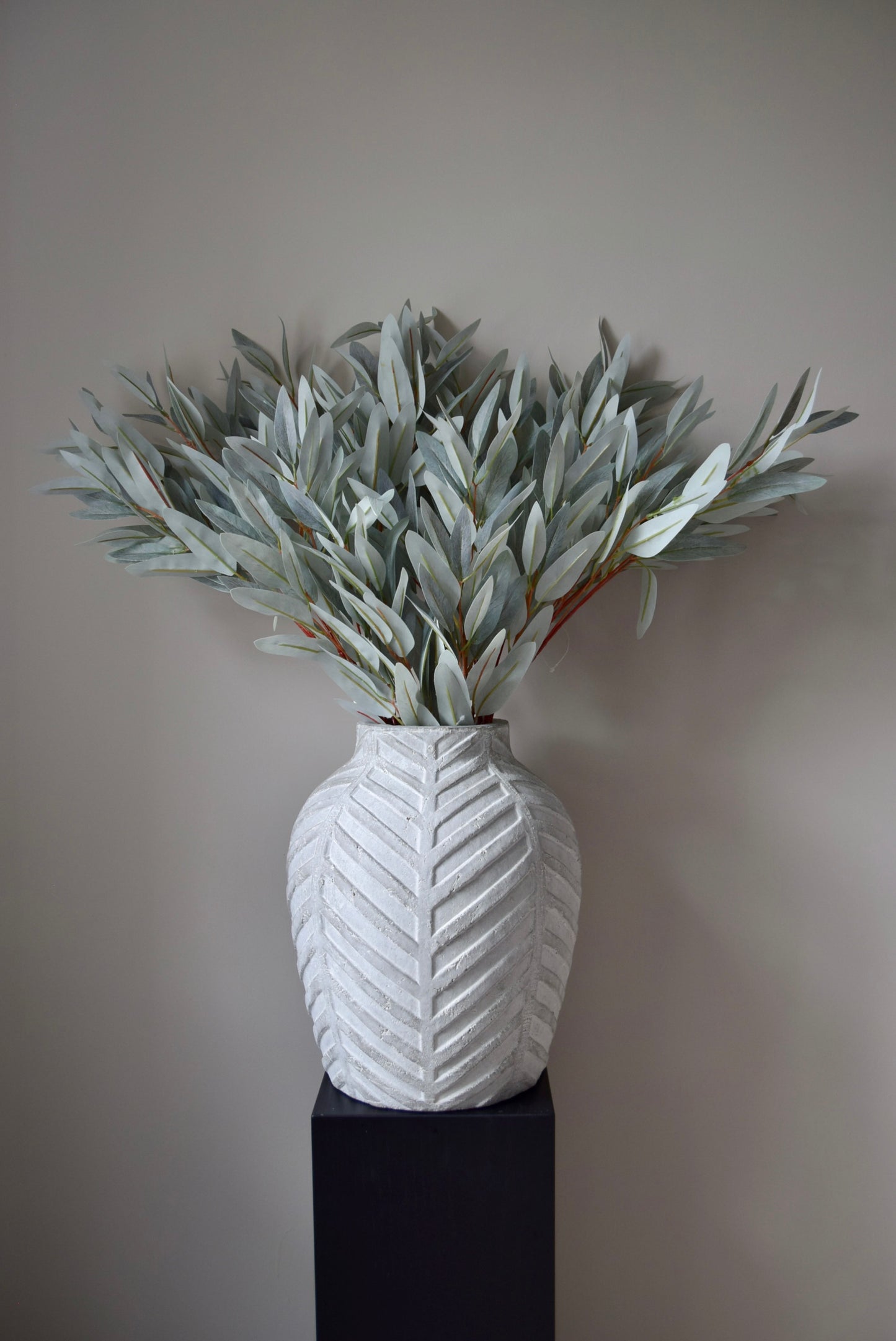 White textured vase with greenery against a plain background