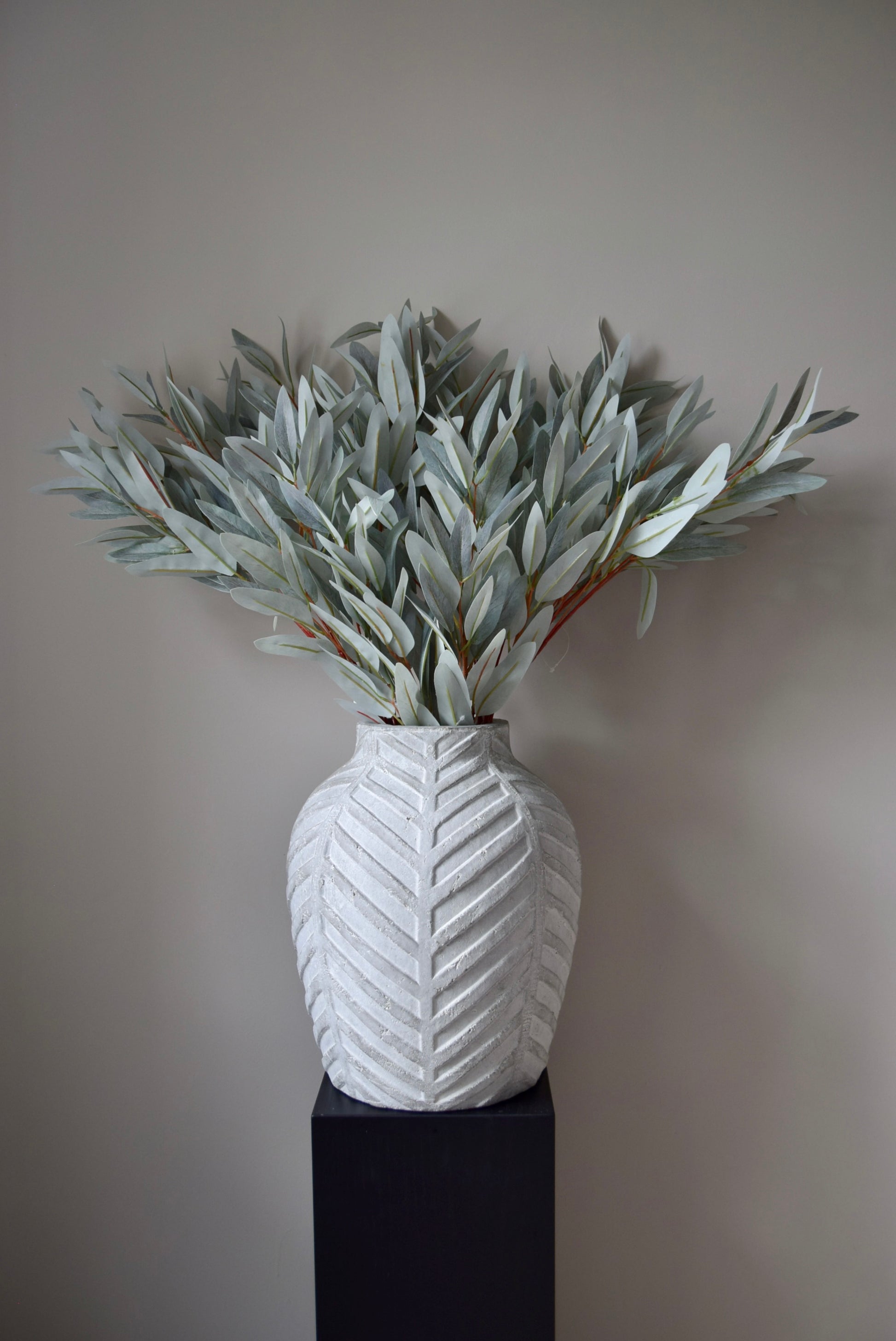 White textured vase with greenery against a plain background