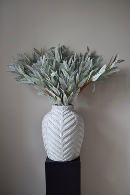 White textured vase with greenery against a plain background