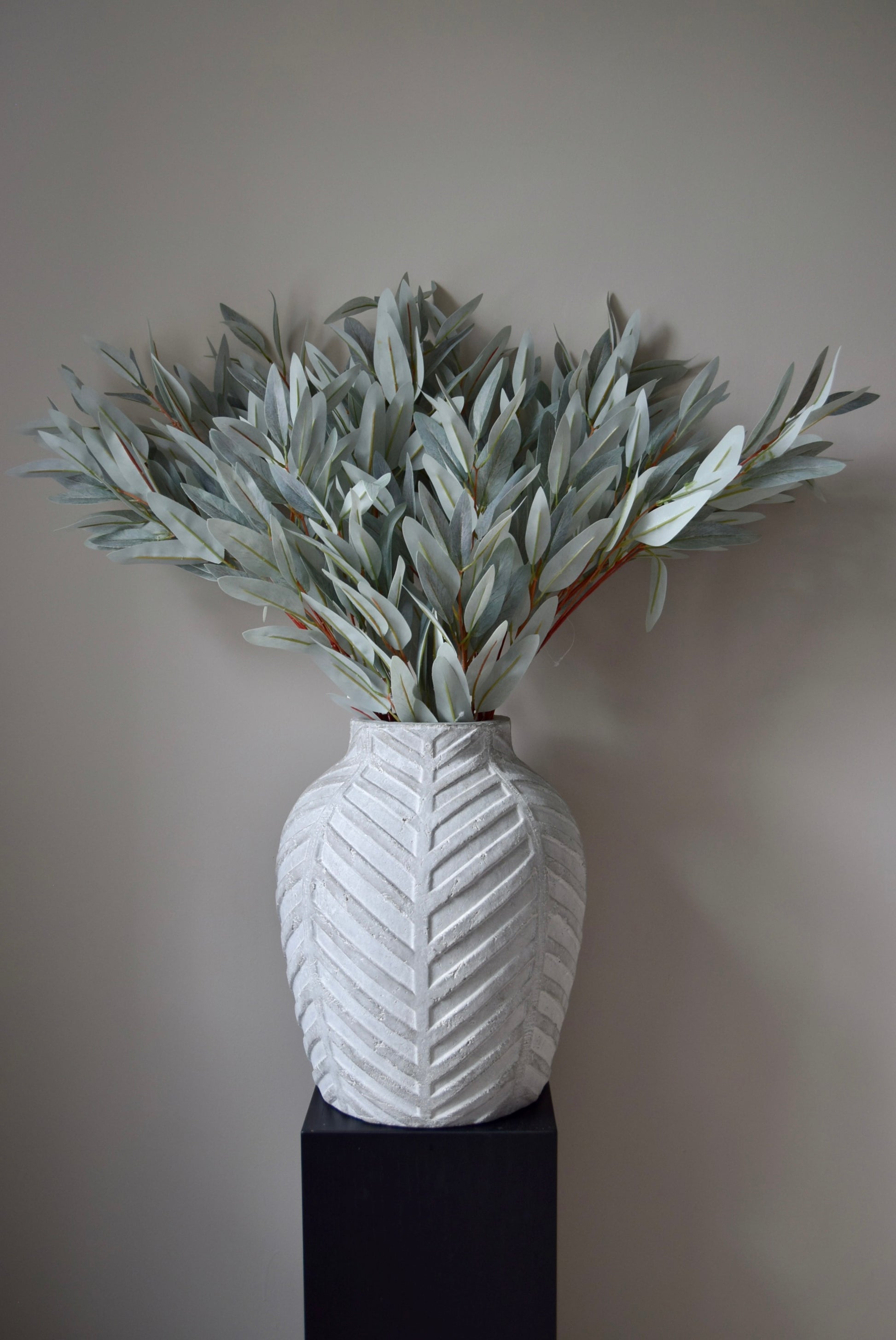 White textured vase with eucalyptus leaves against a plain background