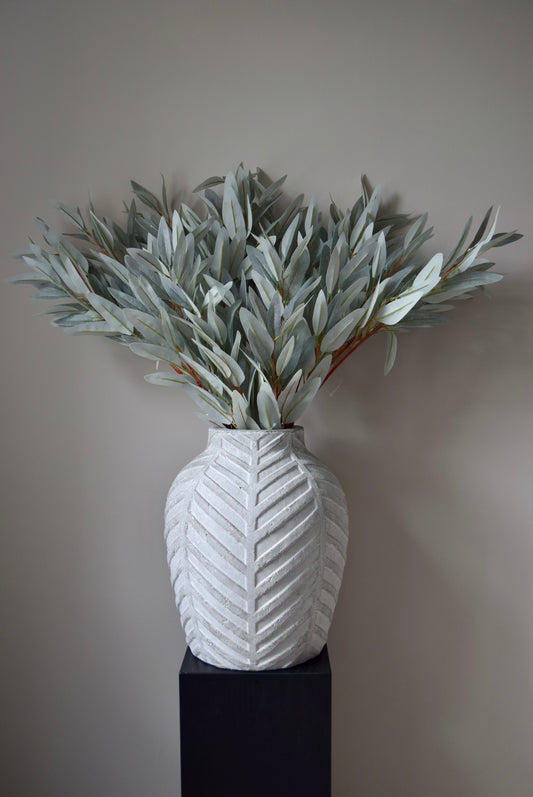 White textured vase with eucalyptus leaves against a plain background