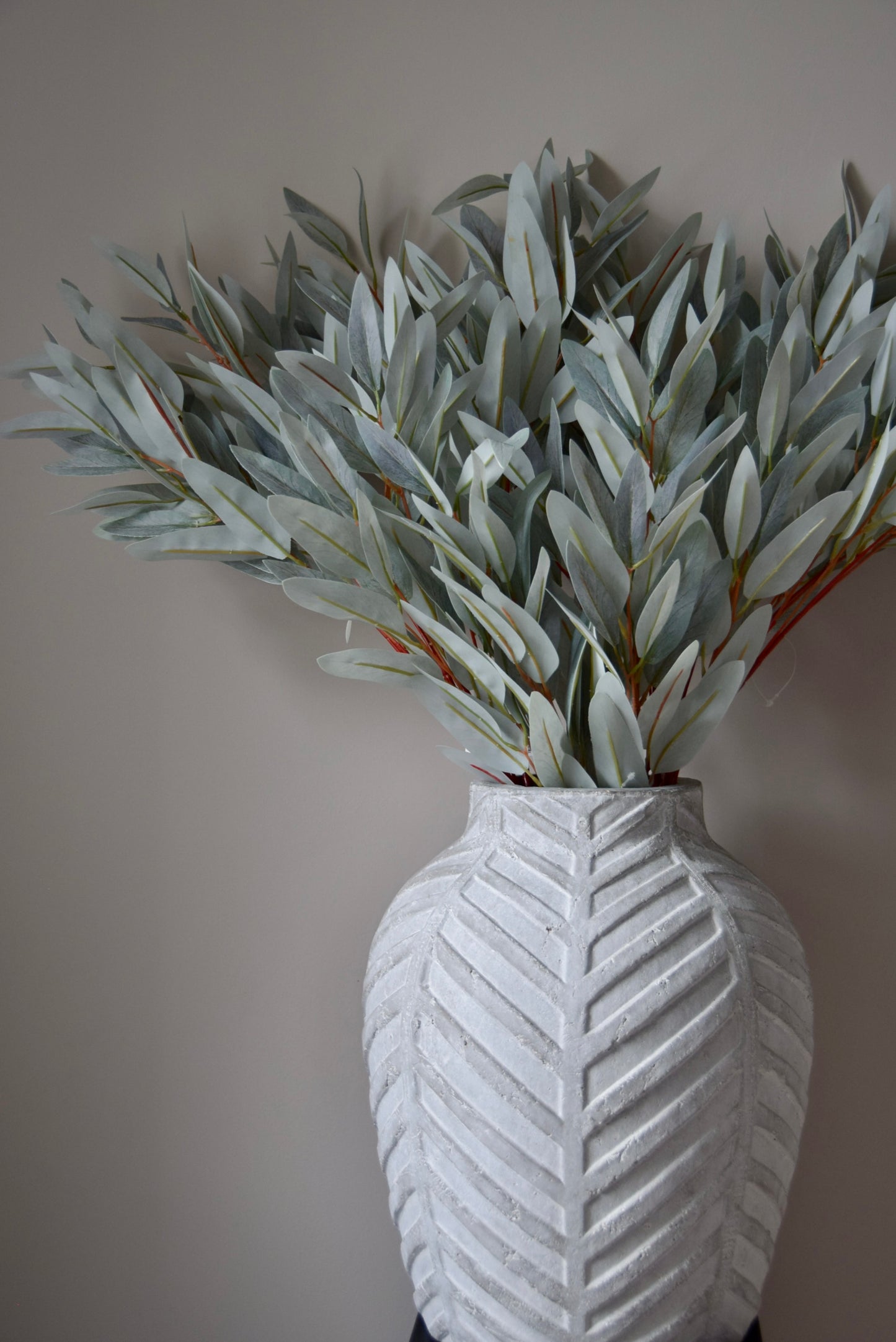 White textured vase with artificial eucalyptus against a plain wall