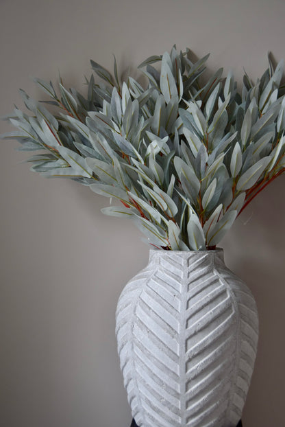 White textured vase with artificial eucalyptus against a plain wall