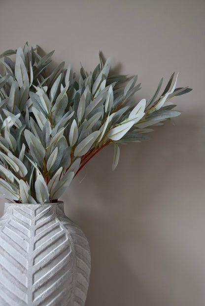 White vase with eucalyptus leaves against a plain wall