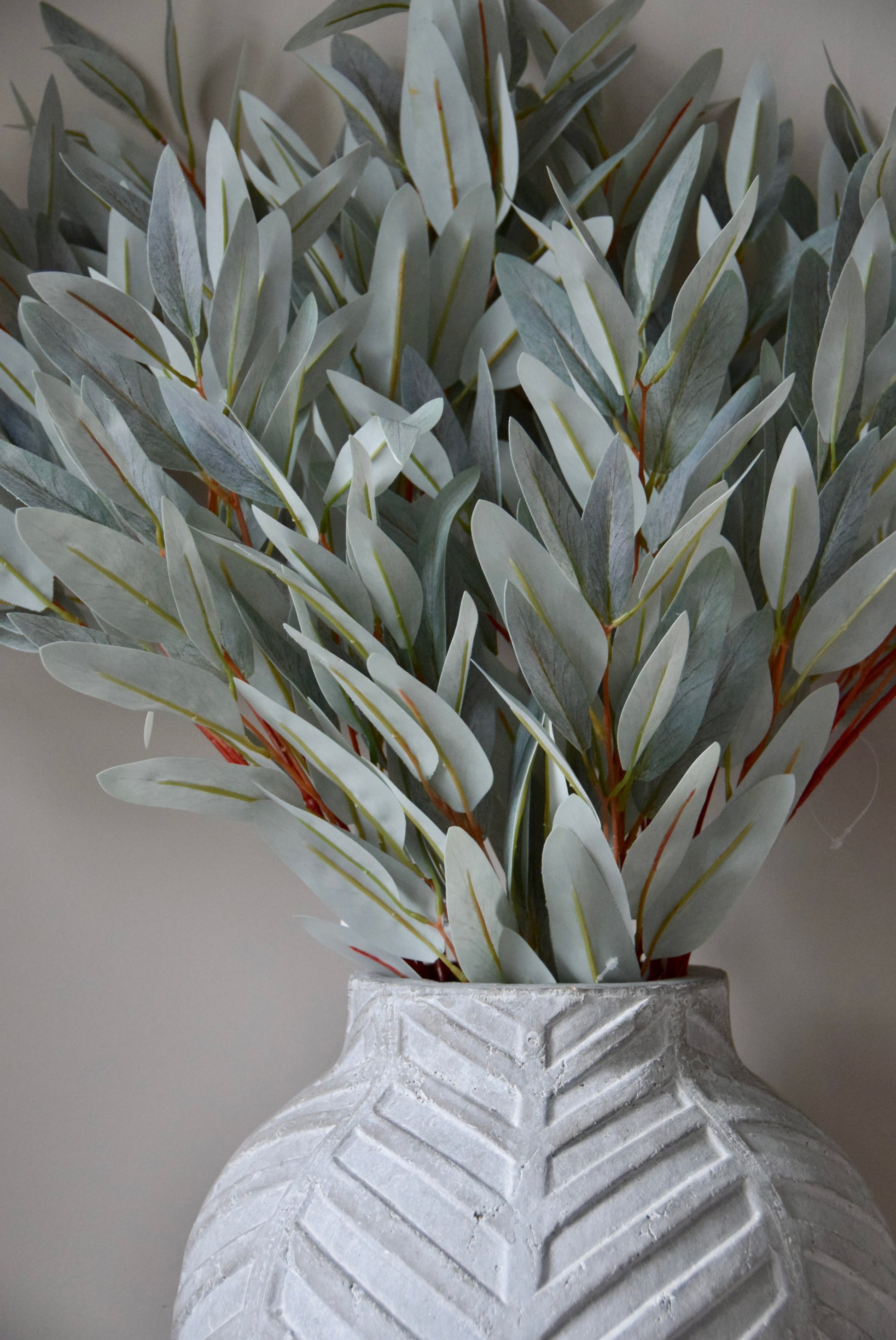 Faux eucalyptus stems in a textured gray vase against a neutral background