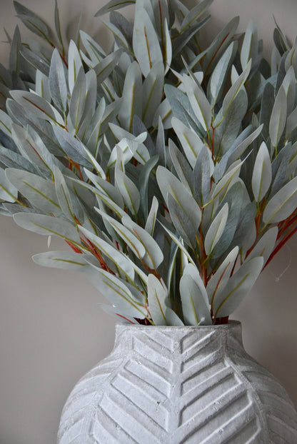 Faux eucalyptus stems in a textured gray vase against a neutral background