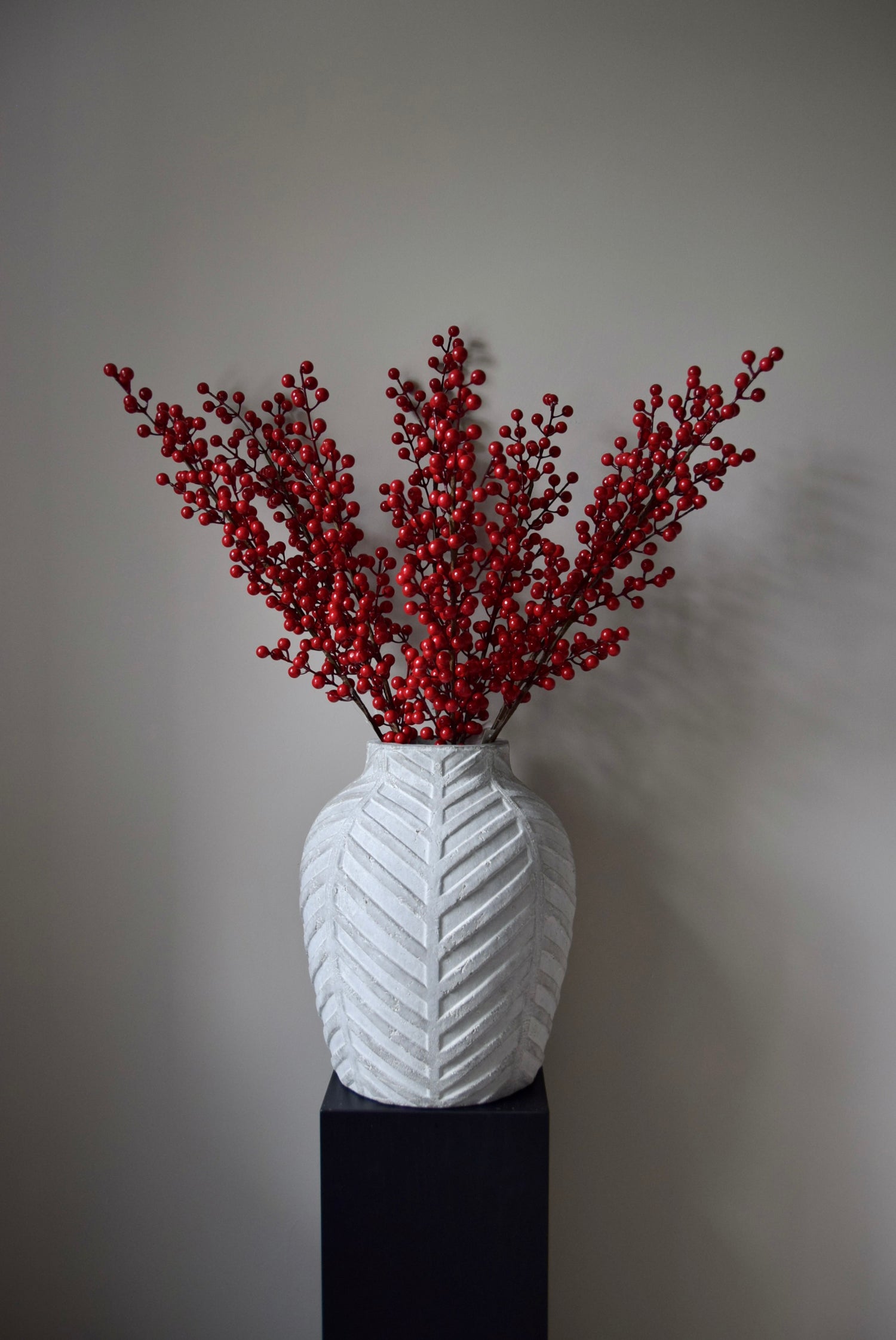 White textured vase with red berries against a grey background