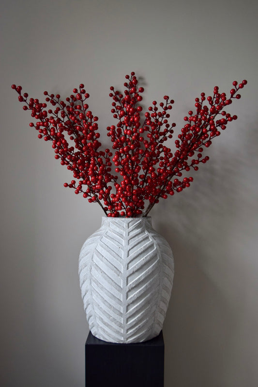 White textured vase with red decorative branches against a grey background