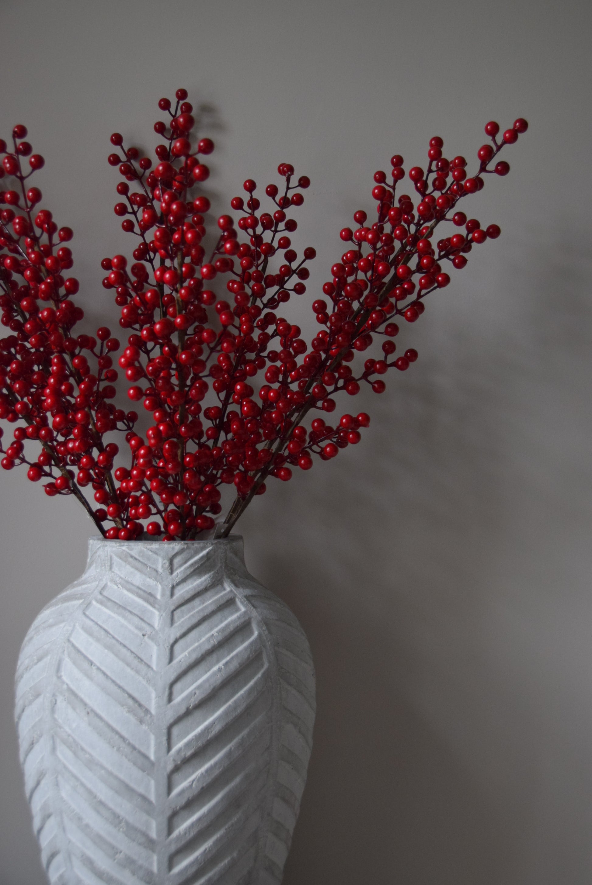 Red decorative branch with a white vase on a grey background