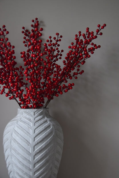 Red decorative branch with a white vase on a grey background