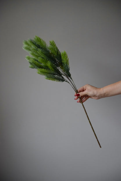 Hand holding an artificial spruce branch against a plain background