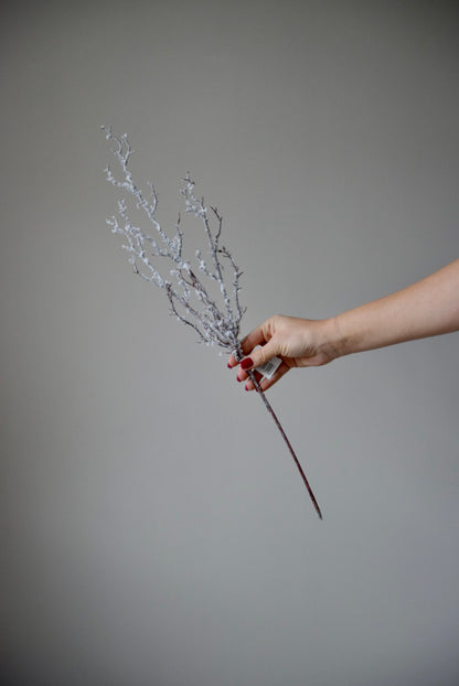 Hand holding a artificial snowy branch against a plain background