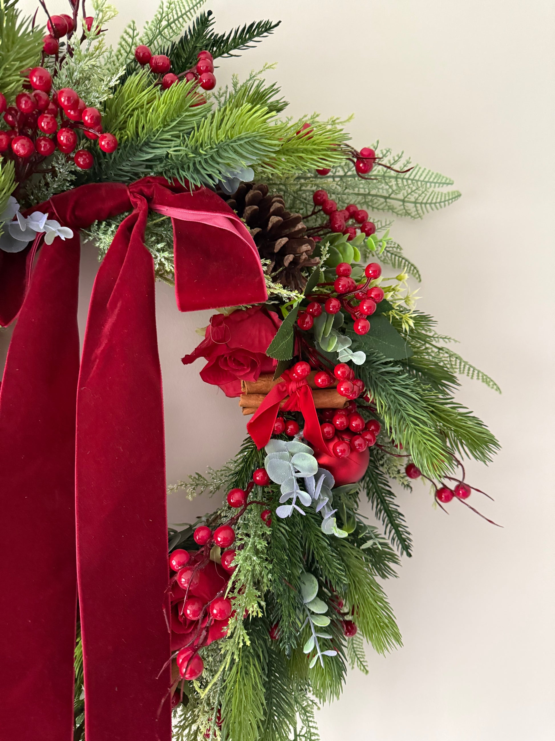 Christmas wreath with greenery, red berries, and a red ribbon on a white background