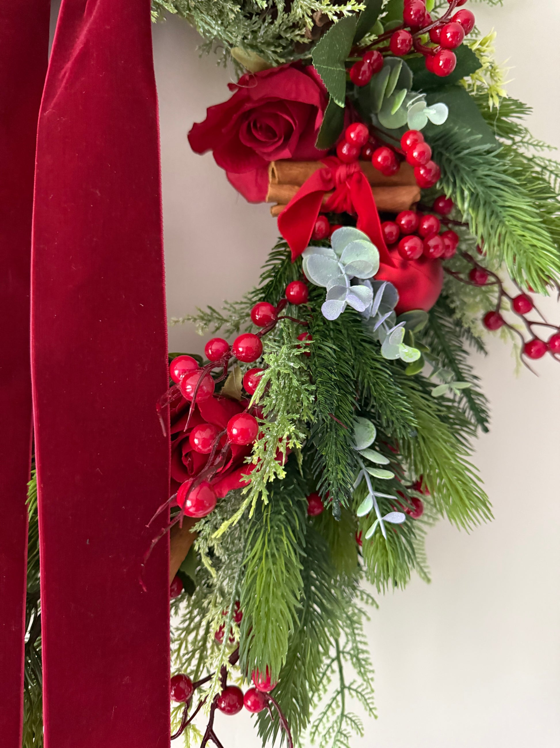 Decorative Christmas arrangement with red roses, berries, and greenery on a white background.