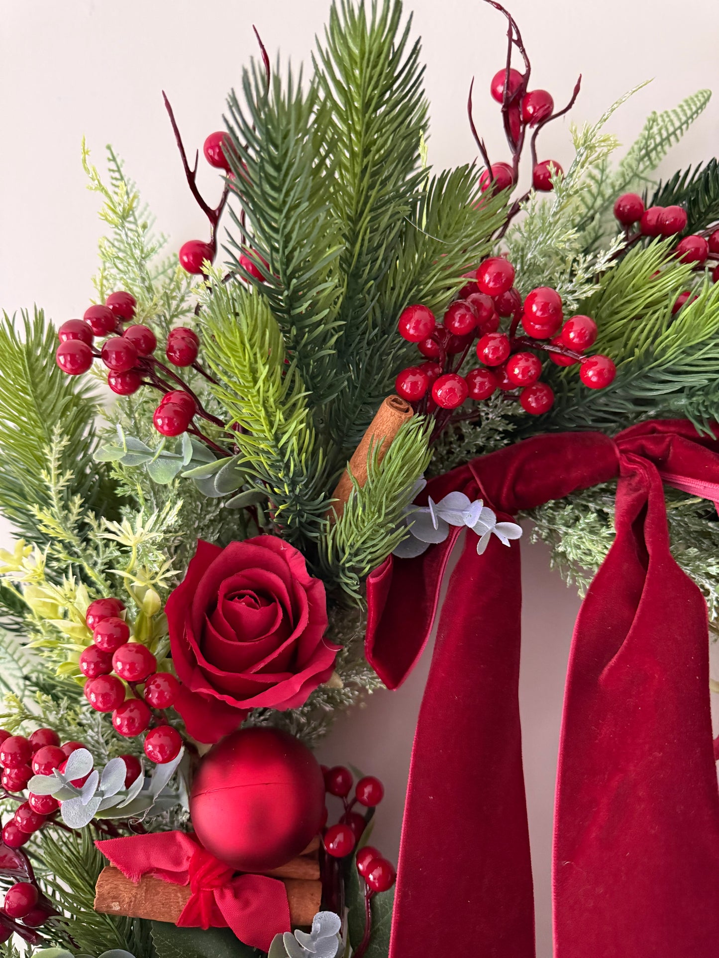 Decorative wreath with red roses, berries, cinnamon sticks, and ribbons on a white background