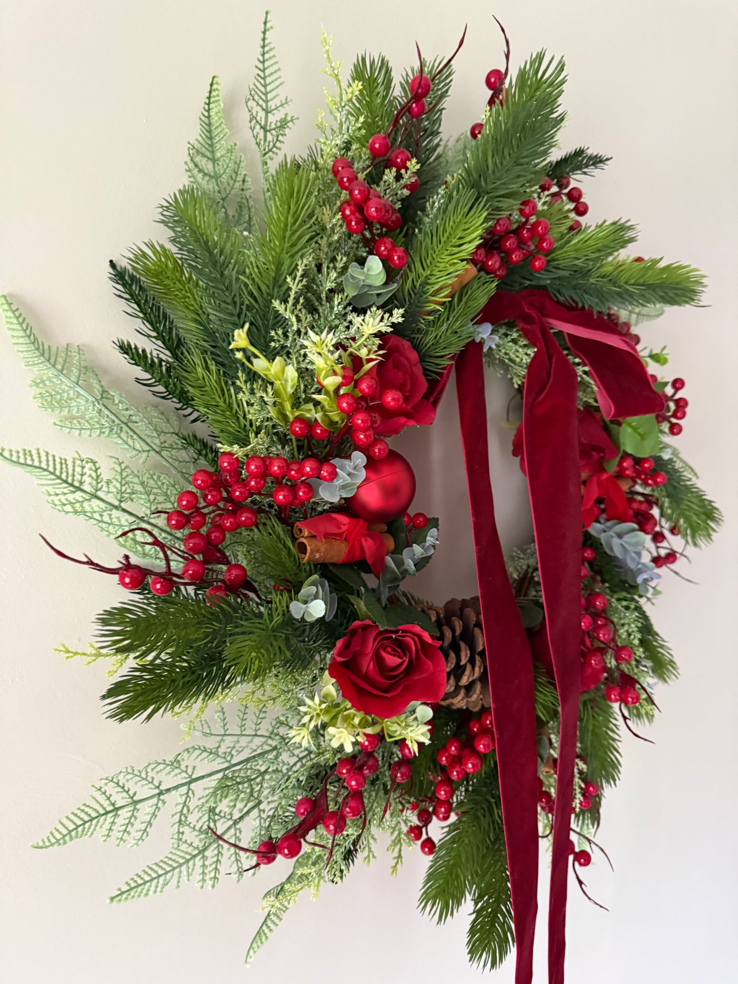 Decorative wreath with greenery, red berries, and a red ribbon on a light background