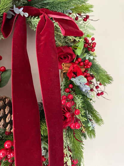 Decorative Christmas arrangement with red ribbons, pine cones, and berries on a white background