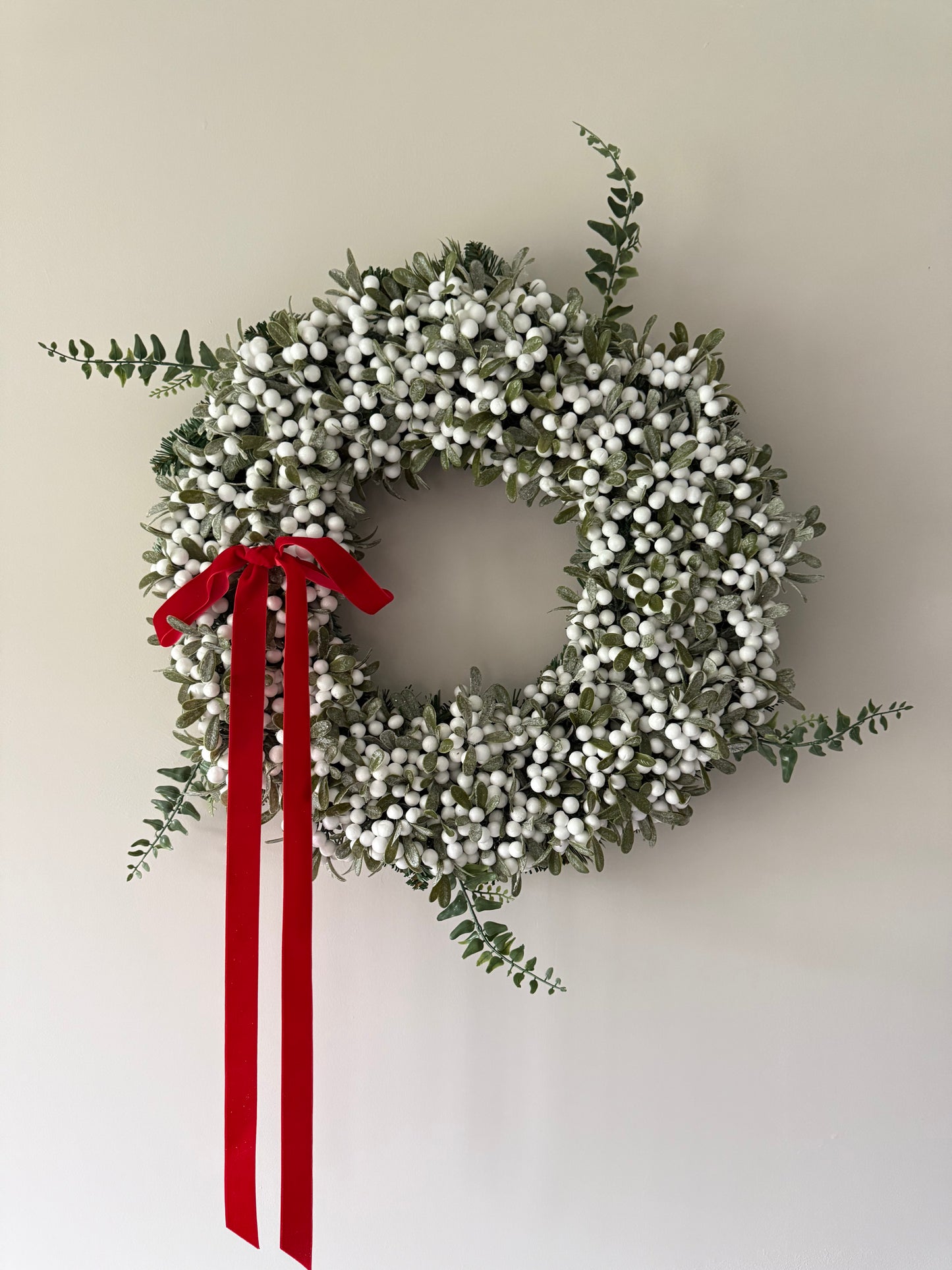 Decorative wreath with white berries and a red ribbon on a plain background