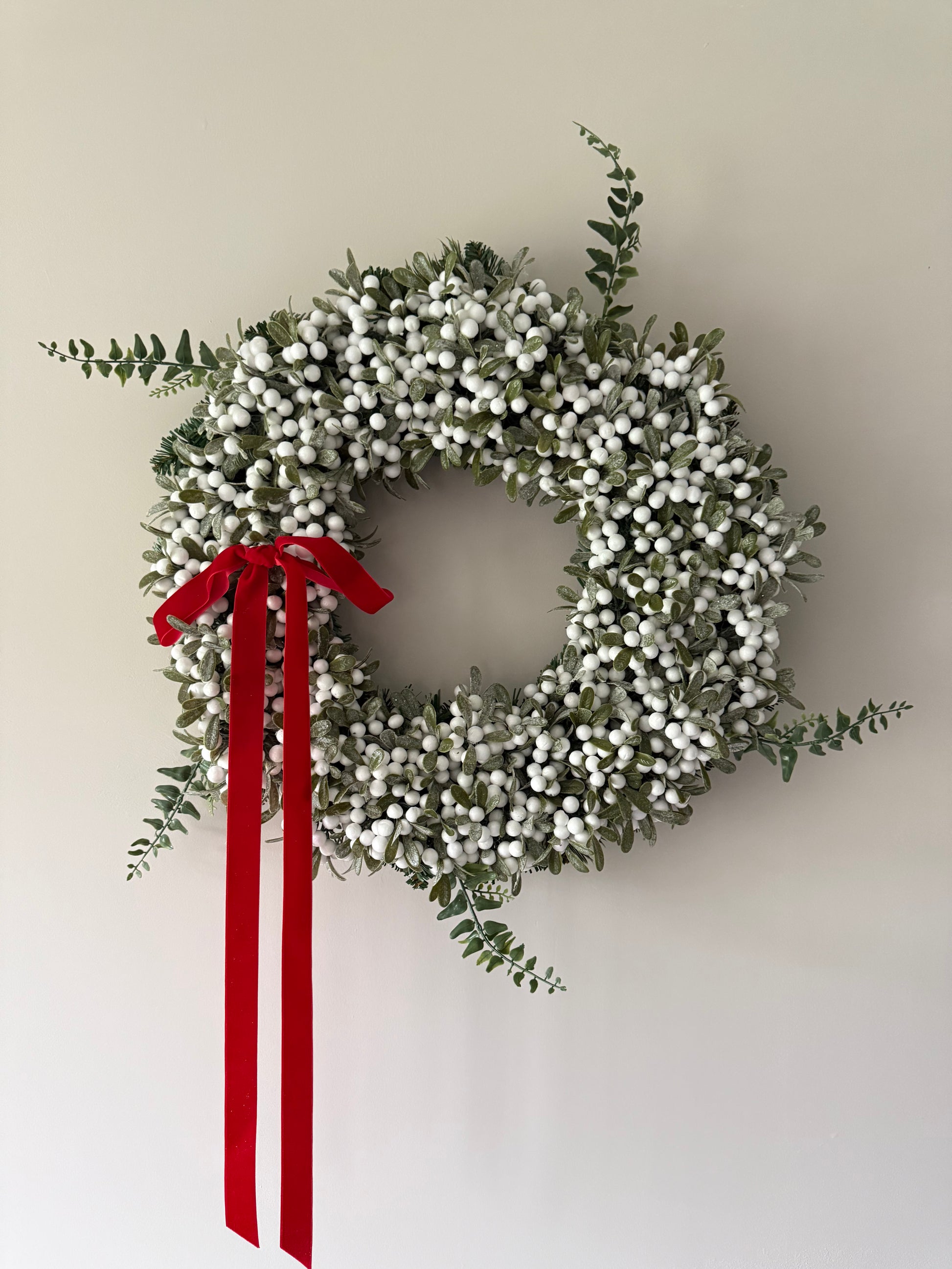 Decorative wreath with white berries and a red ribbon on a plain background