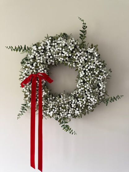 Decorative wreath with white berries and a red ribbon on a plain background
